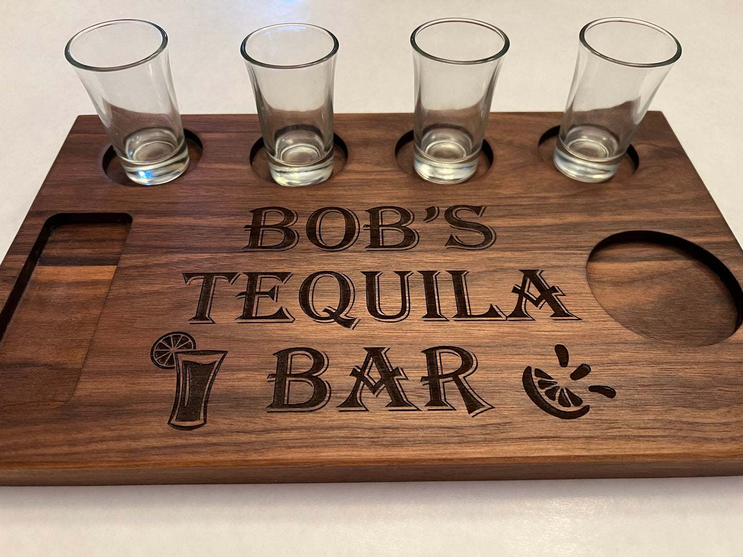 Personalized tequila shot board that reads Bob's Tequila Bar. We will personalize a tequila shot board for you that has first or last name, tequila bar, and a shot glass and a lime. Shot board is made of walnut hardwood.